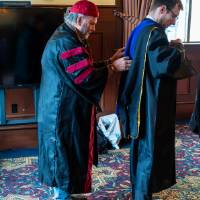 Faculty helping another with gown